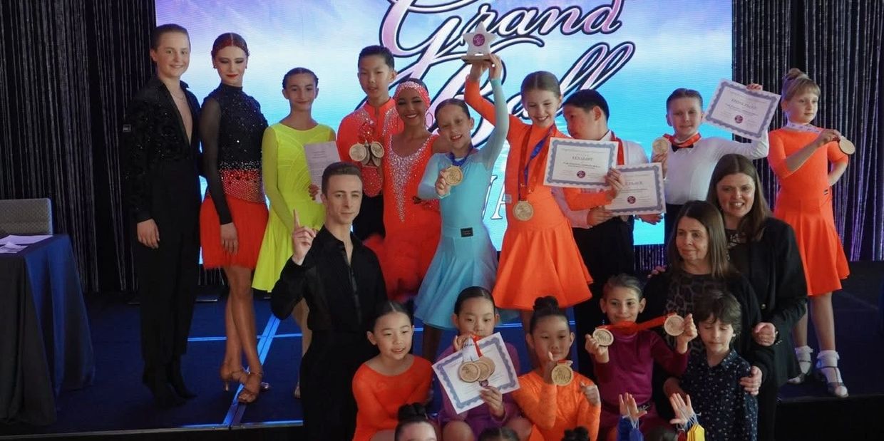 Young dancers proudly display their medals and certificates on stage after a competition.