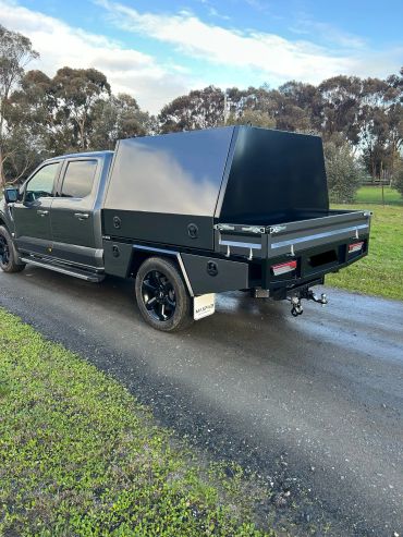 Black pickup truck with custom canopy on a rural road.