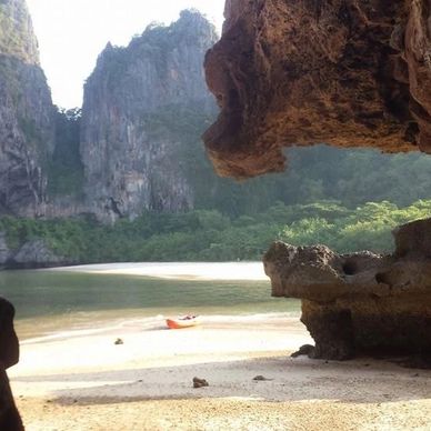 View from a cave opening overlooking a serene beach with cliffs and greenery.