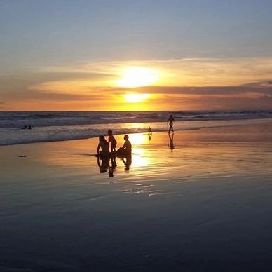 People enjoy a serene sunset at the beach with reflections on wet sand.