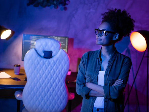 Woman with glasses standing by a computer setup with colorful lighting.