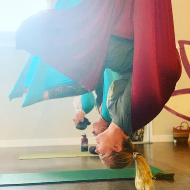 Two people practicing aerial yoga upside down in hammocks indoors.
