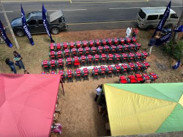 Rows of red machines displayed outdoors with people around tents.