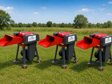 Three red and black wood chippers lined up on grass under a blue sky.