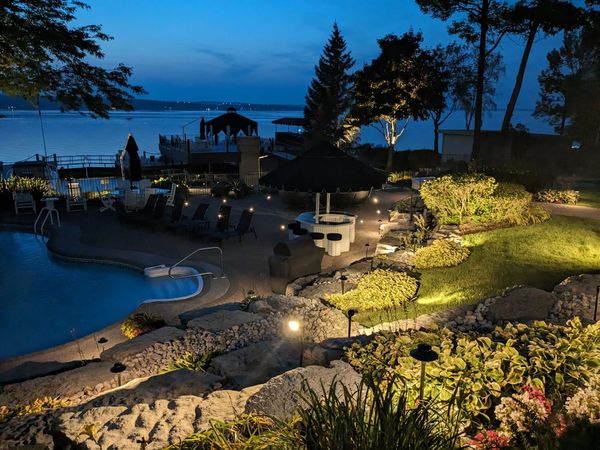 A serene lakeside pool area illuminated at dusk with lush landscaping.