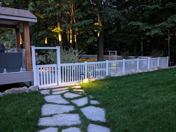 Stone pathway leads to a white picket fence gate in a backyard at dusk.