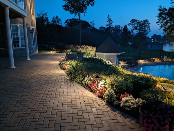 A well-lit garden pathway by a pool at dusk.