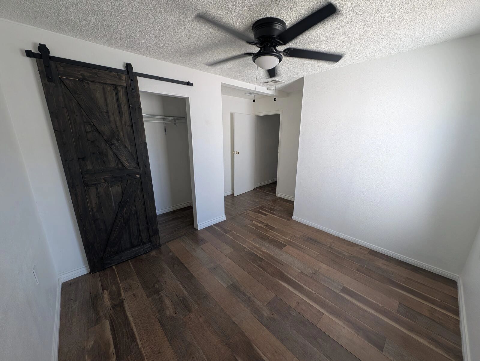 Rental bedroom with a black barn door, ceiling fan and new flooring