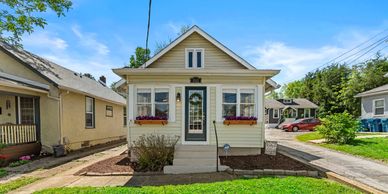 Small beige house with a front porch and flower boxes under the windows.