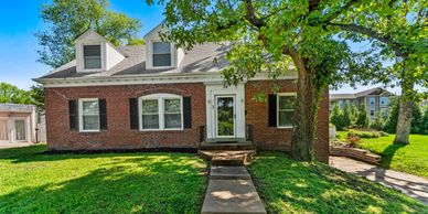 Brick house with dormer windows and a green lawn.