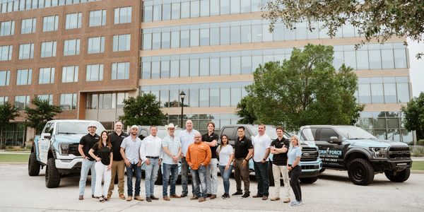 A group of professionals posing in front of branded trucks outside an office building.