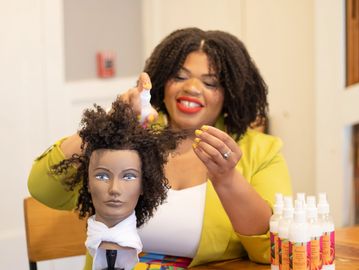 Woman styling curly hair on a mannequin head indoors.