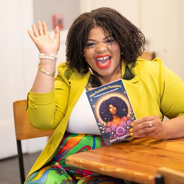 Joyful woman in yellow blazer waving and holding a colorful book.