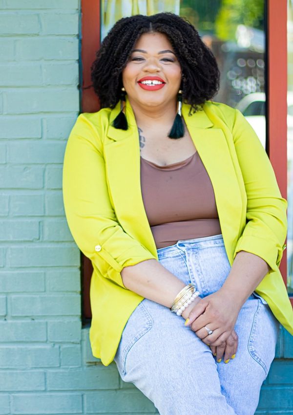 Confident woman in a bright yellow blazer smiling outdoors.