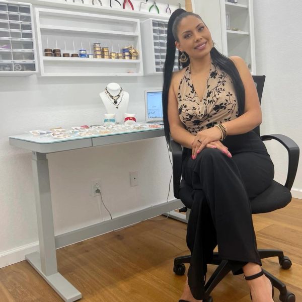 Woman sitting on an office chair beside a jewelry display table.