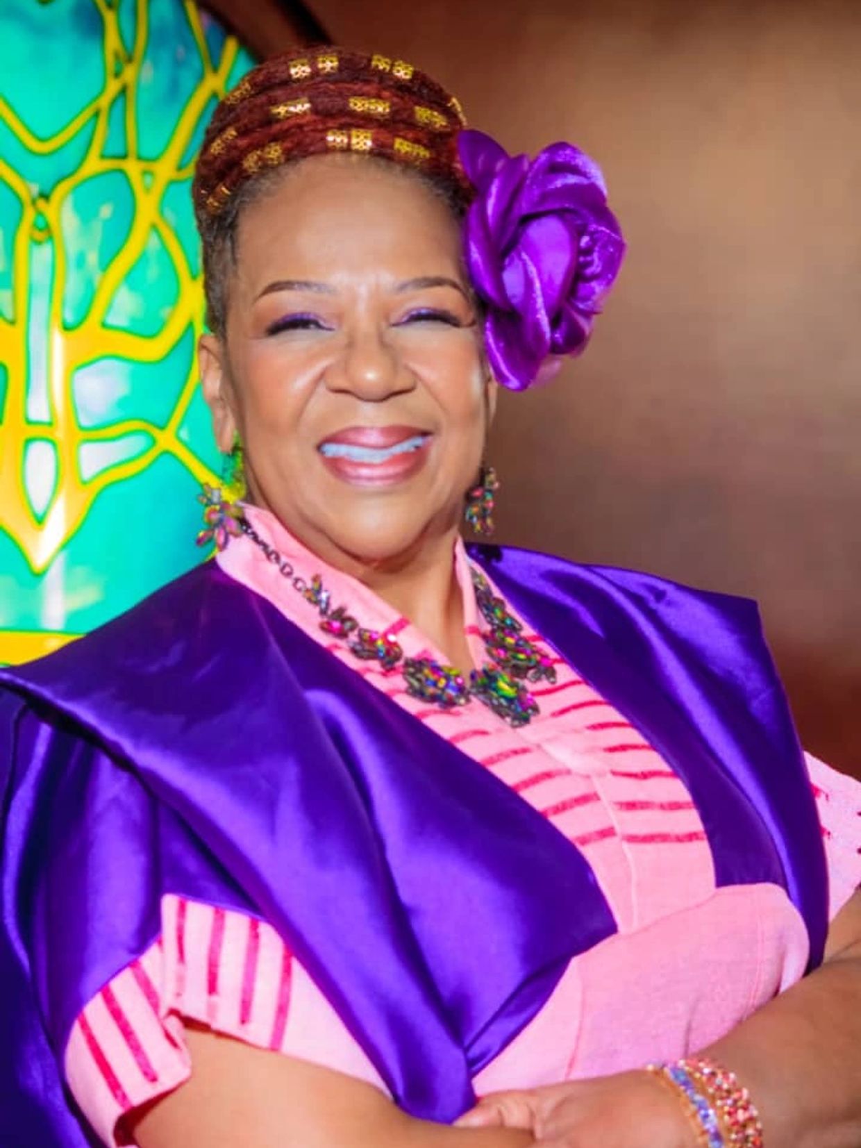 A joyful woman in colorful attire and a purple flower.