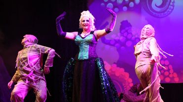 A theatrical performance with a central actress and two dancers in costume.