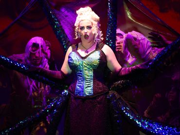 A performer with tentacle-like arms in a dramatic costume on stage.