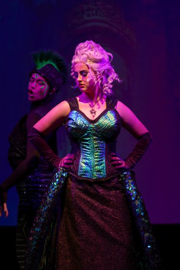 Two performers in elaborate costumes on stage under dramatic lighting.