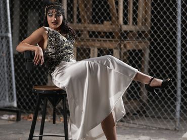 Woman in a stylish dress and headband posing on a chair with a chain-link fence background.