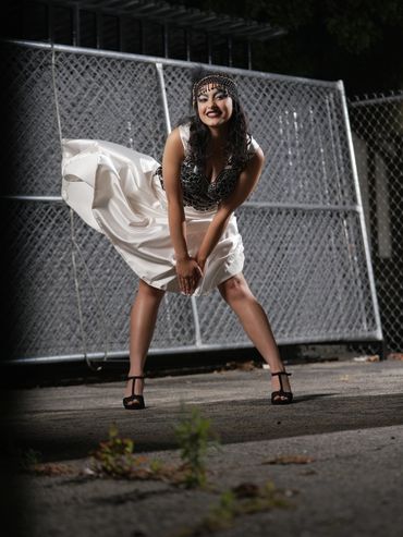 A woman in a stylish dress poses confidently outdoors at night.
