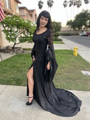 Woman in elegant black gothic dress posing outdoors with a smile.