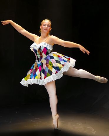Ballet dancer in colorful harlequin costume poses on stage.