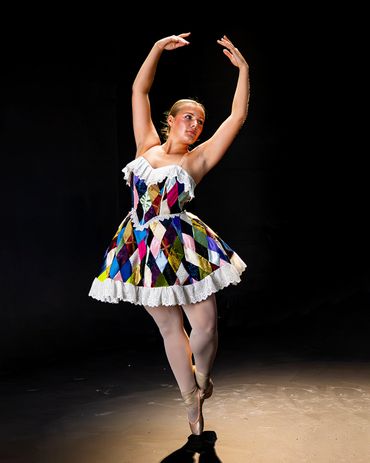 Ballet dancer in colorful costume poses gracefully on stage.