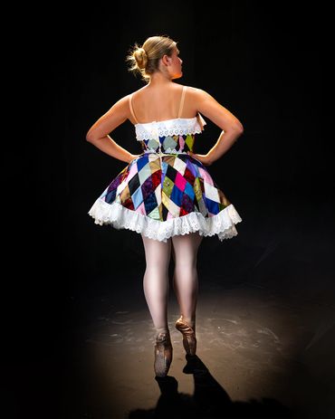 Ballet dancer in colorful costume posing on pointe against dark background.