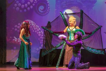 Actors in colorful costumes performing an underwater-themed play on stage.
