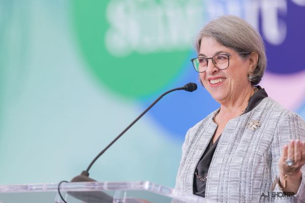 Smiling elderly woman speaking at a podium with microphone.