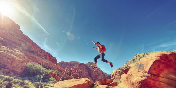 Person jumping between rocky cliffs under a bright blue sky.