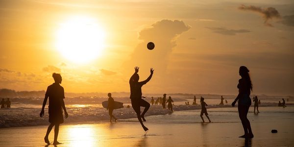 People playing soccer on a beach at sunset.