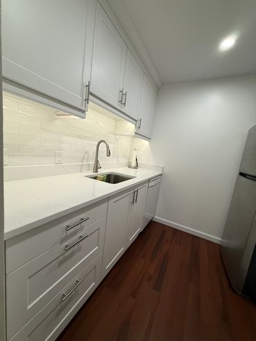 Modern white kitchen with stainless steel appliances and wooden floor.