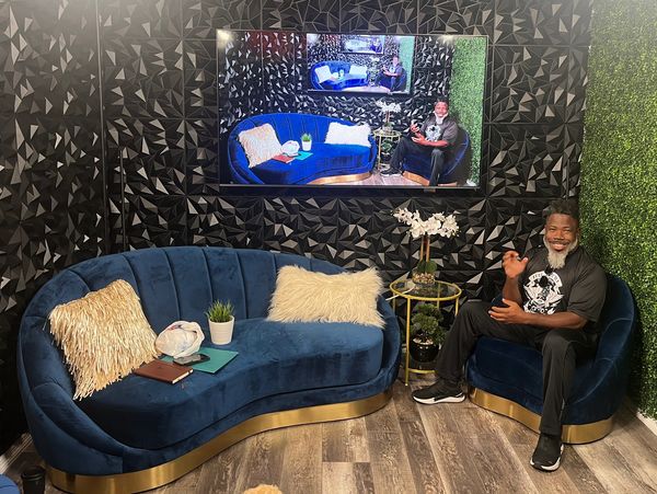 Man sitting on a blue velvet chair in a stylish studio with modern decor.