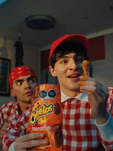 Two men in red checkered shirts, one holding Cheetos and the other looking surprised.