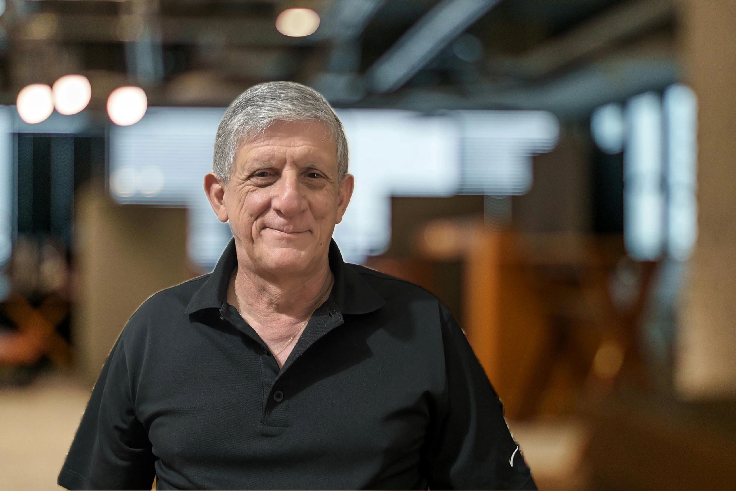 Smiling elderly man in a black polo shirt indoors.