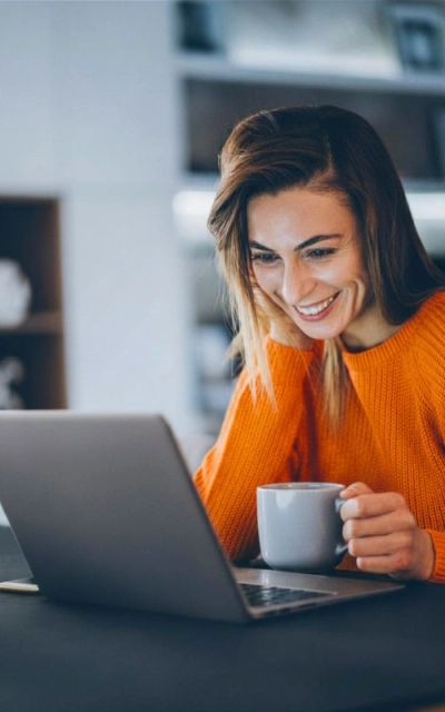 Mujer sonriente usando una laptop con taza en mano.