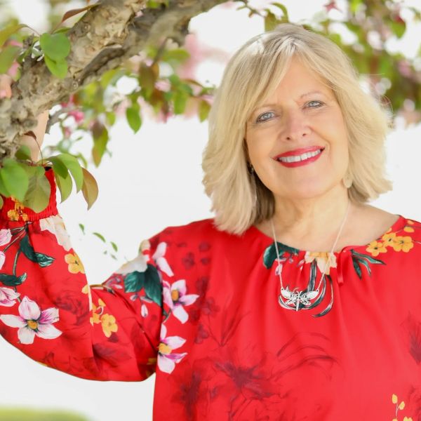 Woman in a red floral dress smiling near a tree.