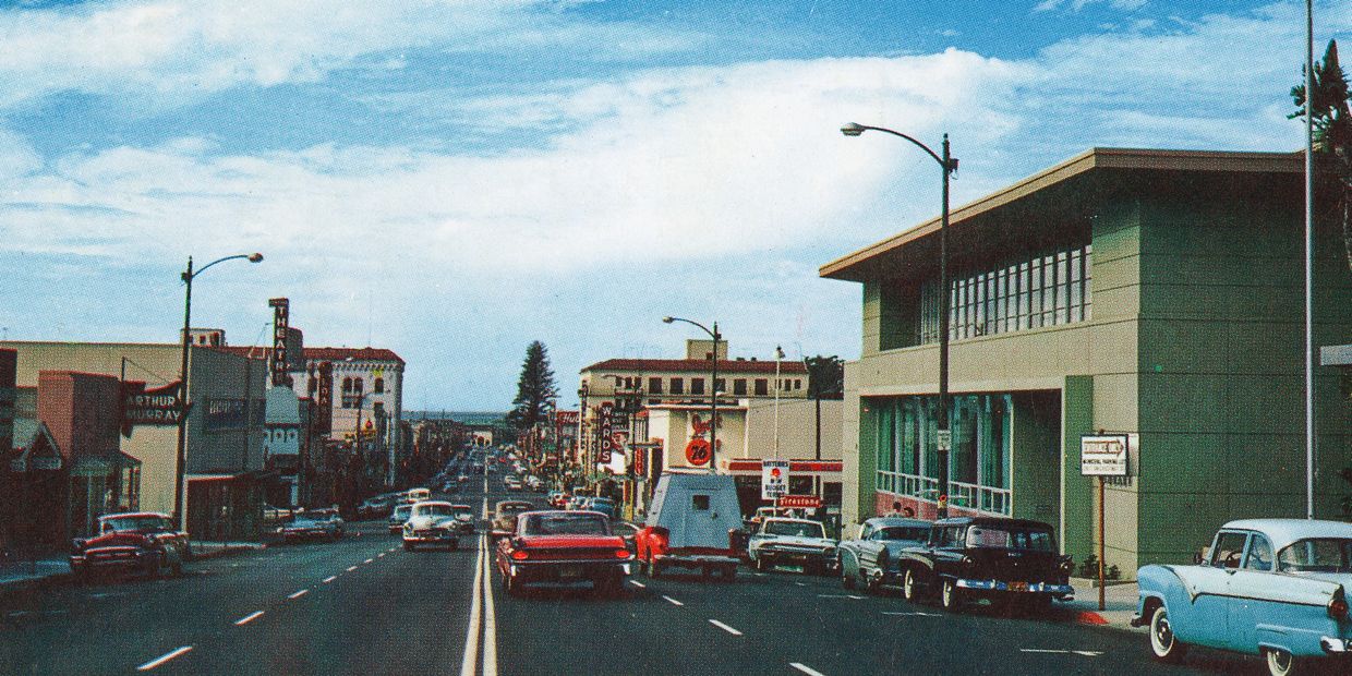 Vintage downtown street scene with classic cars and mid-century buildings.