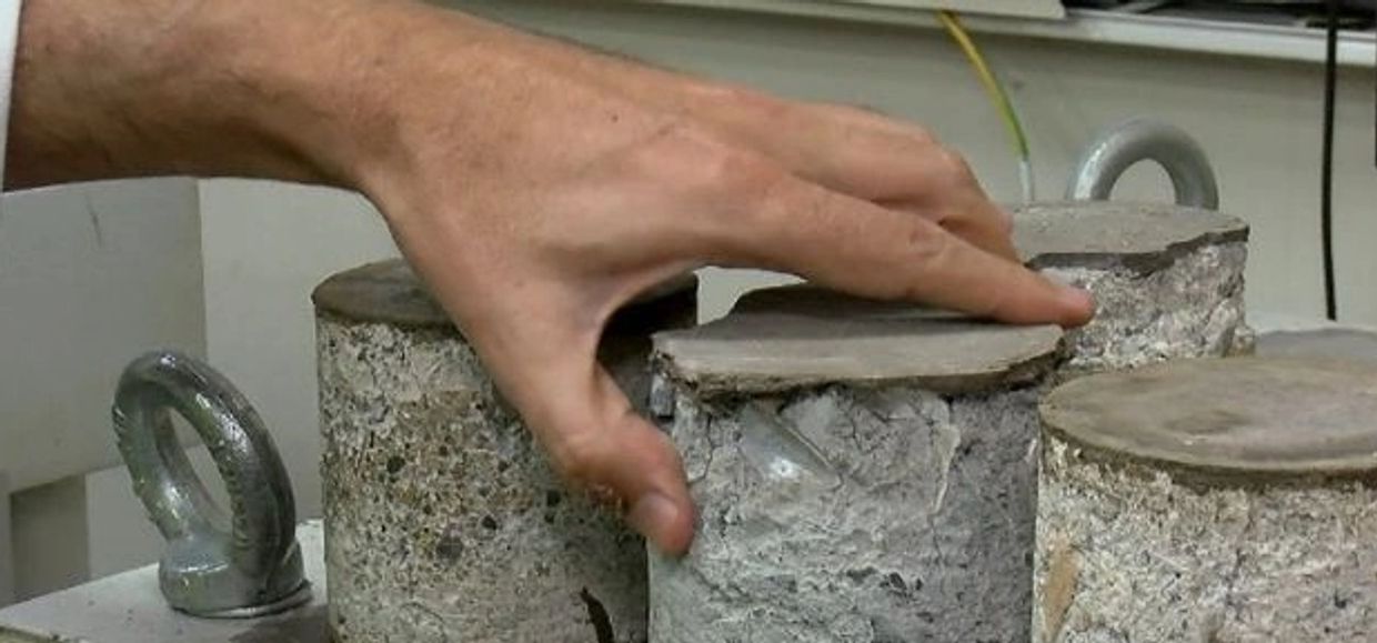 Hand touching cylindrical concrete samples with metal loops on top.