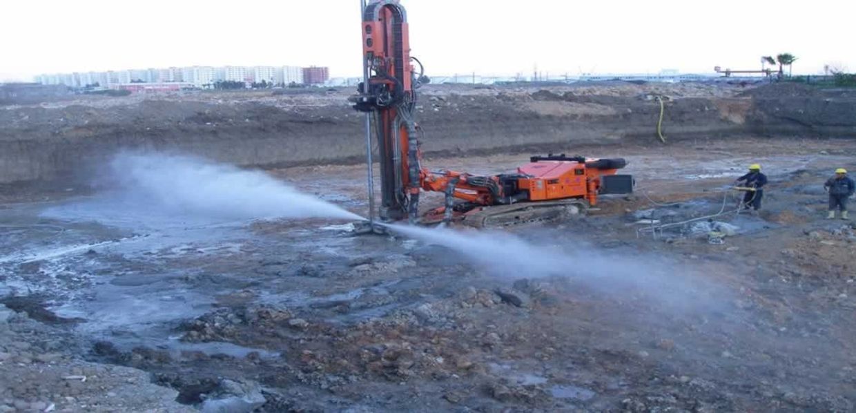 Construction site with machinery spraying water and workers in safety gear.
