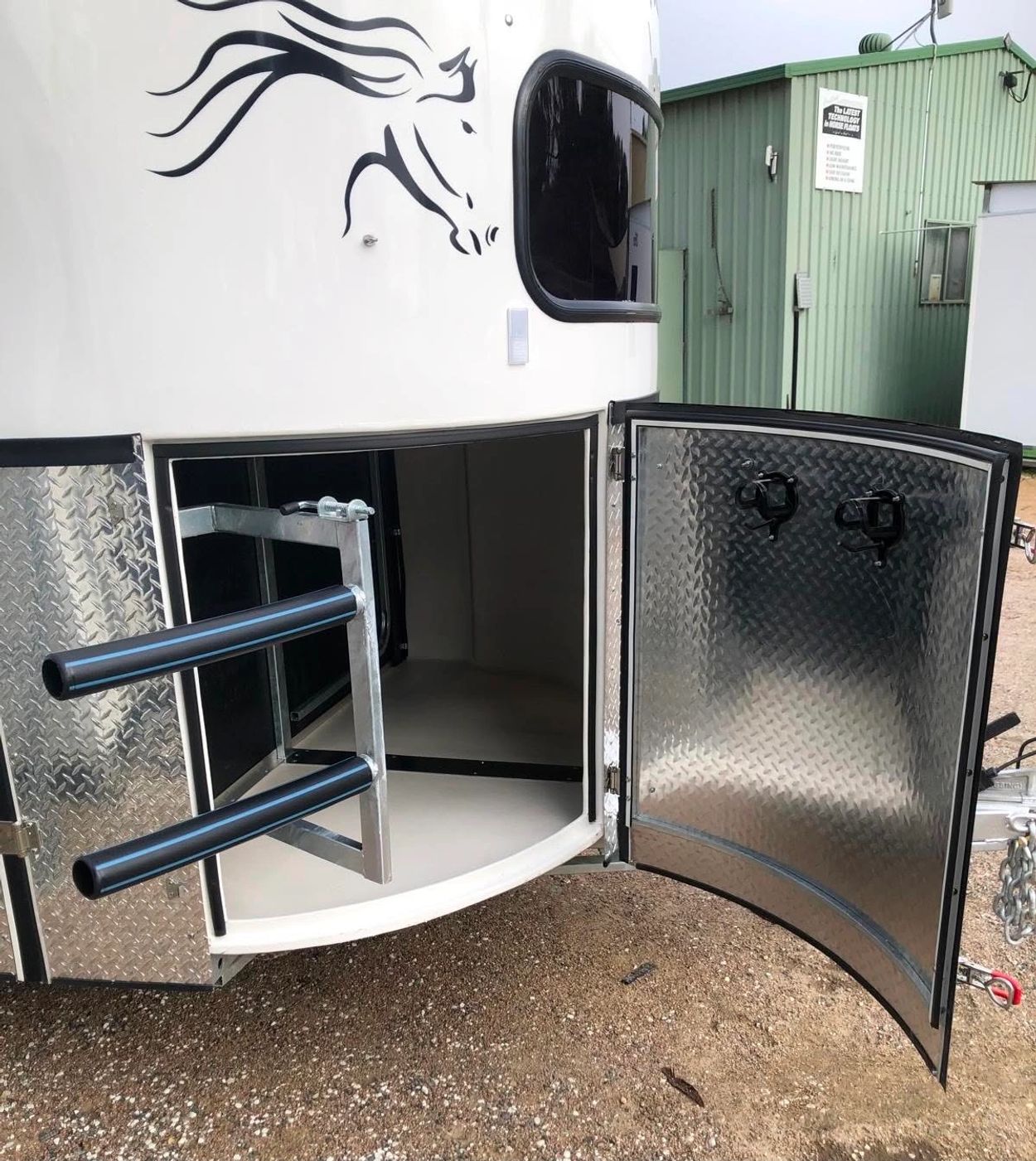 Open storage compartment of a white horse trailer with saddle racks.