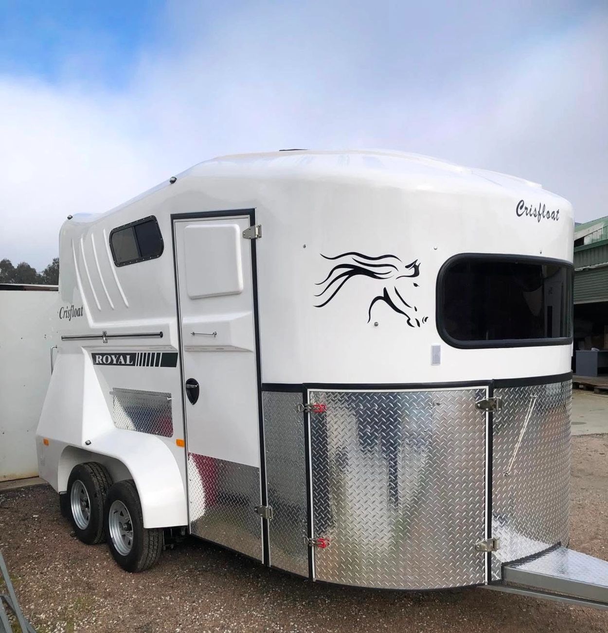 White horse trailer labeled 'Crisfloat' and 'ROYAL' with metal panels and a horse graphic.