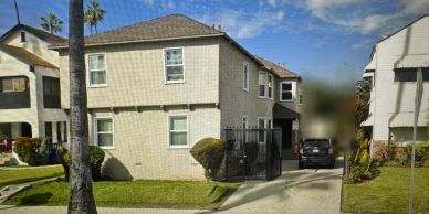 Two-story beige brick house with a driveway and a black car.