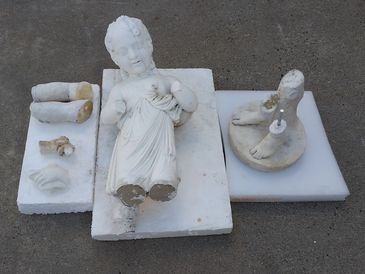 Broken white marble statue of a child with detached limbs on foam blocks.