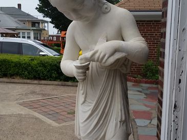 Marble statue of a child holding a bird, placed on a towel outdoors.