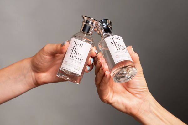 Two hands holding perfume bottles labeled 'Tell Me The Truth'.