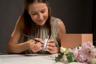 Woman personalizing a perfume bottle with a marker.