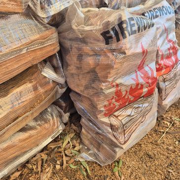 Bags of firewood stacked outdoors with leaf litter on the ground.